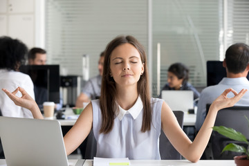 Mindful millennial girl meditating in office taking break for meditation at work, young woman...