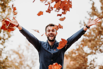 Young man throwing autumn leaves in the air