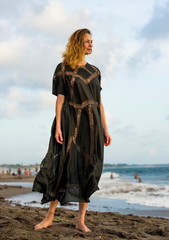 young happy beautiful and glamorous blond woman posing as professional model at the beach wearing stylish dress looking at the sea carefree in holidays travel