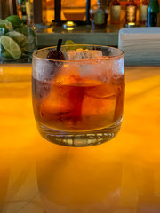 Manhattan whiskey drink with aged cherries on pick, sitting on bar.