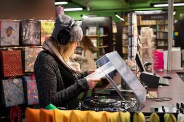 Side view of a girl in warm clothing listening to vinyl record in a book shop.