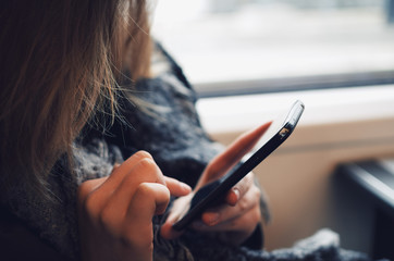 Closeup of a girl in warm clothing using a smartphone in a train.