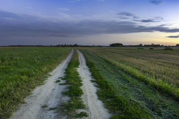 Country road through fields, clouds after sunset