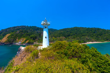 Fototapeta na wymiar A white lighthouse stands on a hill of the peninsula in front of the cliffs and tropical island with dense green forest on a clean sunny cloudless day. Lanta National Park Lighthouse, Krabi, Thailand.