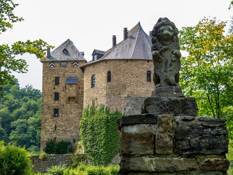 A lion statue at the exterior entrance to Reinhardstein Castle, Burg Reinhardstein in Ovifat, Belgium, the castle in the background