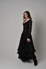 Fototapeta premium full length portrait of brunette girl wearing long black gown with corset. standing pose on grey studio background.