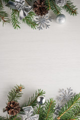 Vertical shot of green spruce twigs, pine cones and silver Christmas decorations on white background with copy space