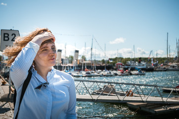 A portrait of a beautiful girl in light blue shirt standing in a sunny seaplane harbour.