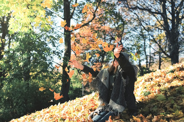 Girl having fun by throwing colourful autumn leaves in a sunny park.