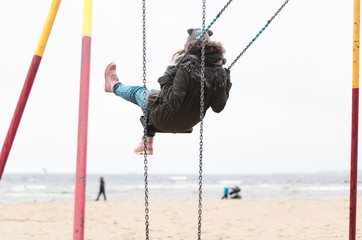 Happy girl having fun swinging at the beach during fall season.