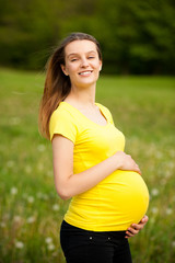 gnant woman in yellow t shirt on a green meadow in spring