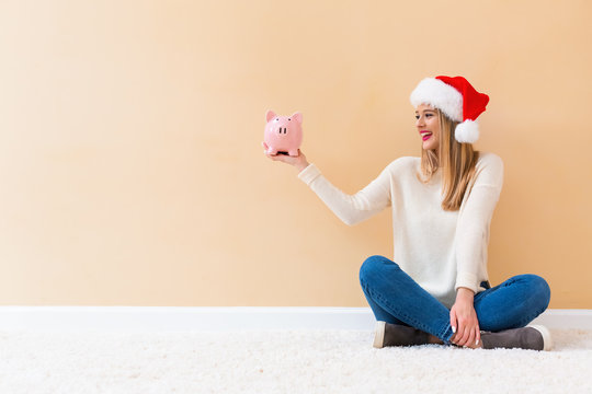 Young woman with santa hat holding a piggy bank on a white carpet