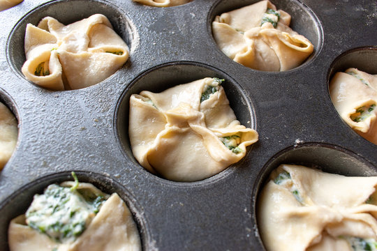Unbaked spinage and cheese filling in puff pastry dough shells in muffin tin