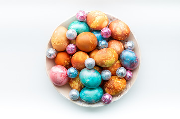 Top view of colourful dyed easter eggs in ceramic bowl on a white background.