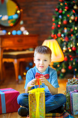 Fototapeta na wymiar happy boy sitting on the floor and holding his presents, on the background of the lights of a festive Christmas tree, Christmas morning
