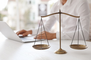 Scales of justice and blurred notary with laptop on background