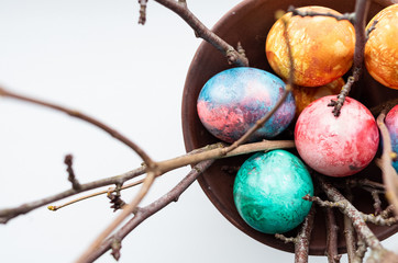 Top view of colourful dyed easter eggs on a white background with ament branches in a vase.