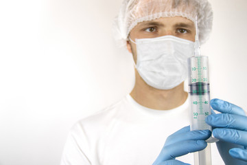 A young guy in a medical mask and hat is holding a medical syringe in front of him