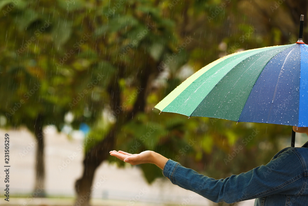 Wall mural Woman with bright umbrella under rain on street, closeup