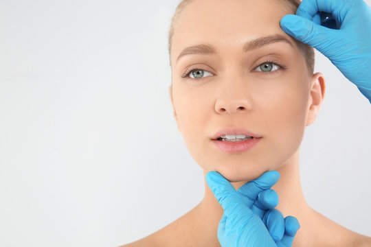 Doctor examining young woman face before cosmetic surgery on white background