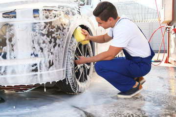 Worker cleaning automobile with sponge at car wash