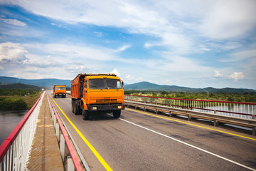 Two orange dump trucks moving over the bridge