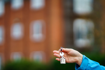 Hand holding house key in front of a large house.
