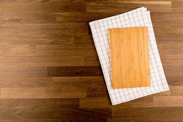 Cutting board on white kitchen towel with left side copy space, on wooden background. Top View
