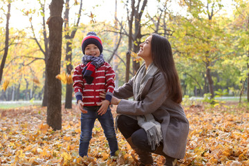 Mother with her cute son spending time together in park. Autumn walk