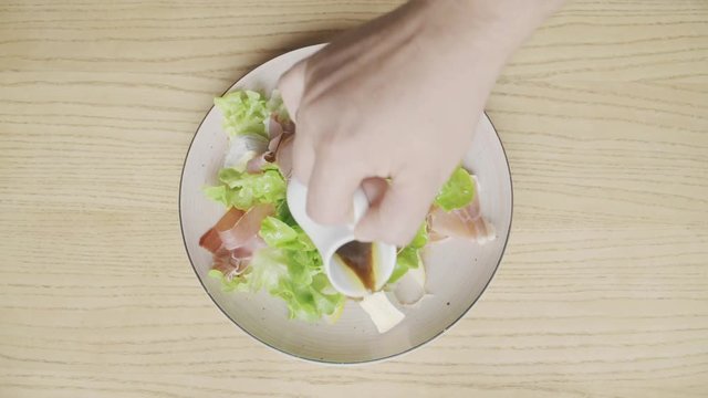 Male hands pours sauce on salad on wooden table, top view