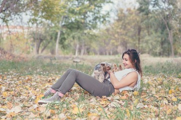 Beautiful young girl with her Yorkshire terrier dog puppy enjoying in the autumn day in the park...