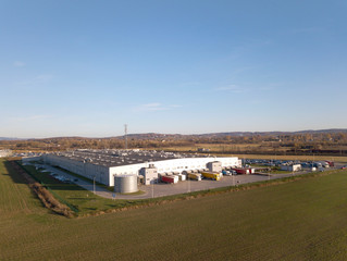 A bird's-eye view of a factory located among green fields. Aerial photography of an industrial facility from a drone or quadrocopter. Transportation of goods to the warehouses of the enterprise.