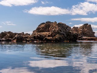 Rocks and blue sky reflections in the Irish Sea on a calm and sunny summer day at the seashore.