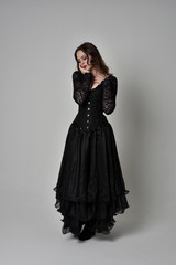 Fototapeta premium full length portrait of brunette girl wearing long black gown with corset. standing pose on grey studio background.