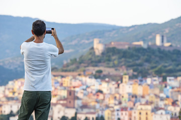 A tourist is taking a picture with his phone at the beautiful and colorful village of Bosa  located in the north-west of Sardinia, Italy.