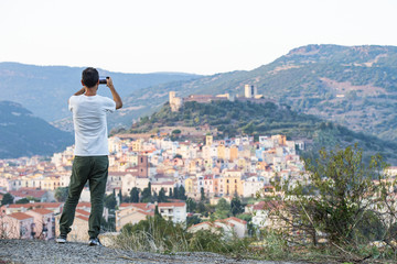 A tourist is taking a picture with his phone at the beautiful and colorful village of Bosa  located in the north-west of Sardinia, Italy.