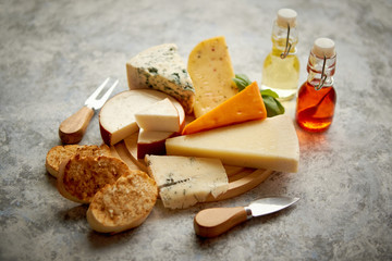 Various types of cheese served on rustic wooden board. Placed on concrete background.