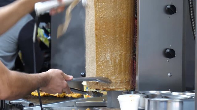 Two unrecognizable men working at takeaway shop or takeout restaurant, slicing doner kebab meat roasting on vertical rotisserie
