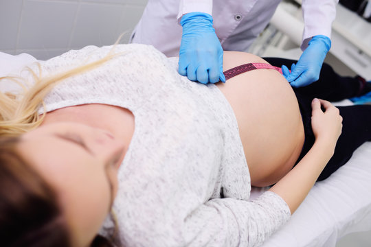 doctor gynecologist examines a pregnant woman with a large belly against a modern clinic
