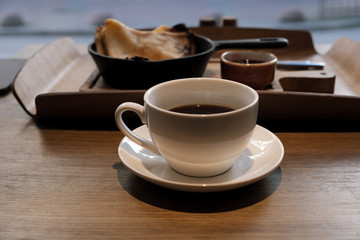 A cup of coffee and pancakes in a cast iron pan.