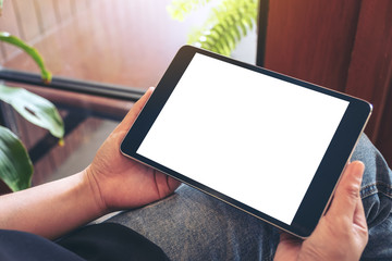 Mockup image of a woman holding black tablet pc with blank white screen while sitting in cafe
