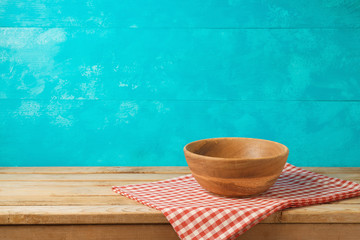 Empty wooden bowl on kitchen table with tablecloth over blue background