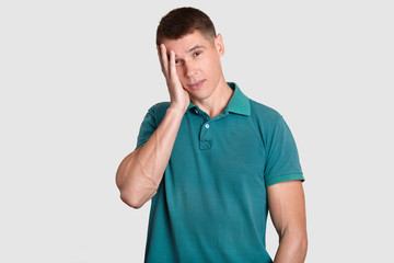 Perplexed European man keeps hand on head, looks with frustrated expression at camera, has some...