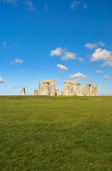 Stonehenge Monument, England. Iconic Great Britain place. Blue sky with clouds in background. Green field in close up