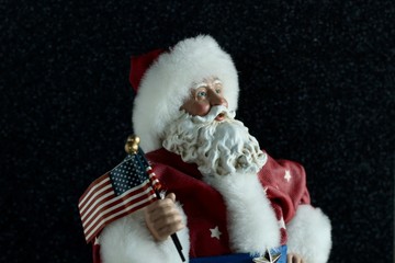 patriotic Santa Claus wearing red white and blue suit holding the American flag on a black...