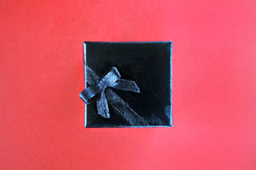 Gift box wrapped in black paper with black ribbon on red beckground. Copy space and top view. Black friday box gift present.