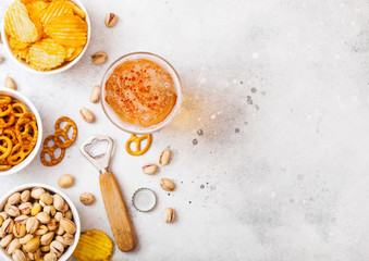 Glass of craft lager beer with snack and opener on stone kitchen table background. Pretzel and crisps and pistachio in white ceramic bowl. Space for text