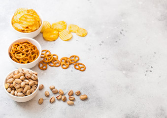 Pretzel and potato crisps and pistachio in white ceramic bowl on stone kitchen table background. Space for text. Snack for beer