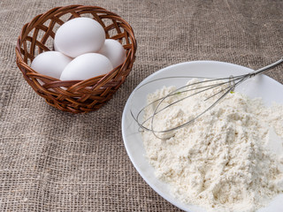 Basket with eggs and a plate of flour on a wooden background