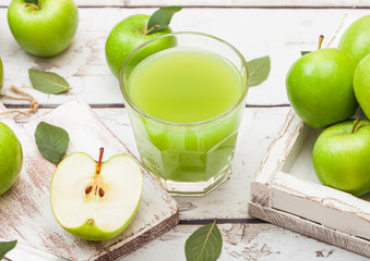 Glass of fresh organic apple juice with green apples in box on wooden background